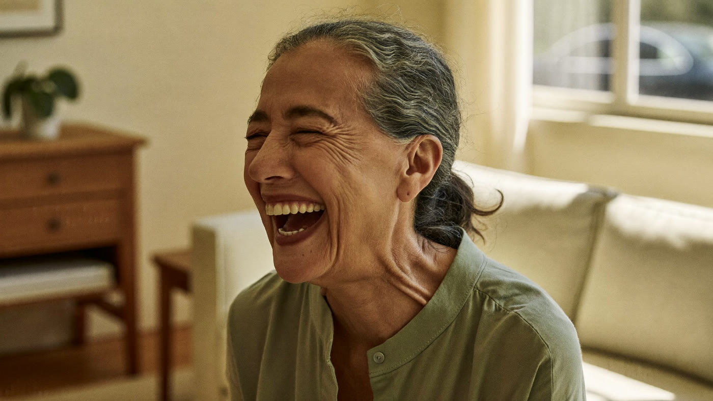 A woman laughing warmly in a sunlit living room