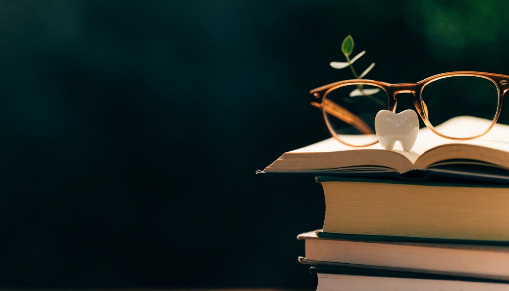 Books, reading glasses and a tooth representing a dental implant guide