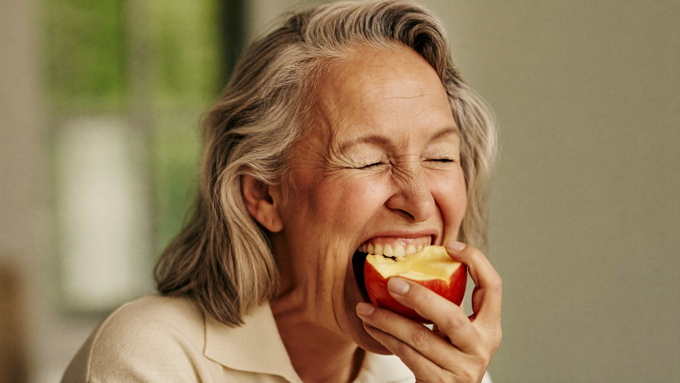 A woman in her sixties biting confidently into a fresh apple