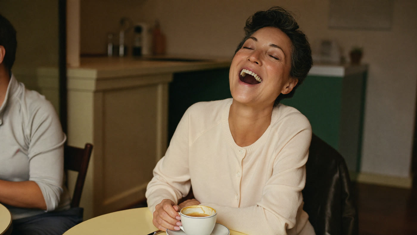 A woman laughing openly over coffee with a friend